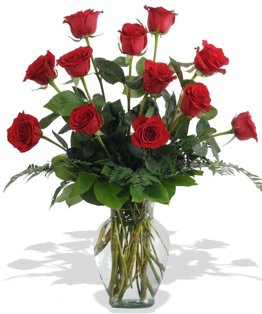 Dozen red roses in the vase, complimented by seasonal greenery