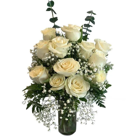 Dozen white roses in the vase, complimented by seasonal greenery