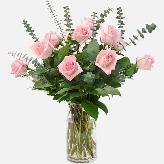 Dozen pink roses in the vase, complimented by seasonal greenery